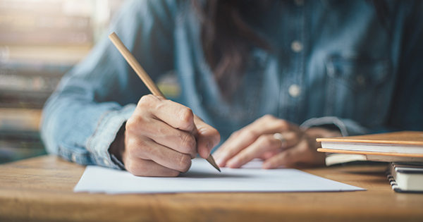 Hands holding pencil writing paper answer sheet.