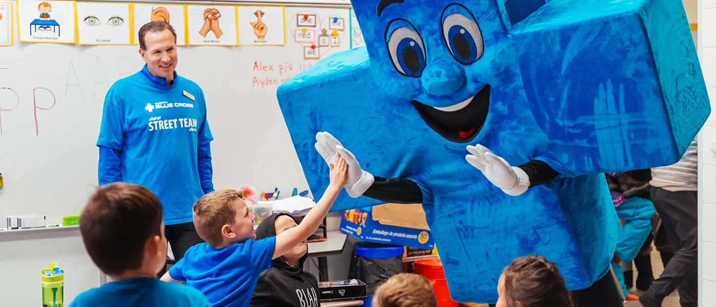 Alberta Blue Cross® mascot, Big Blue, is high-fiving children in their classroom.