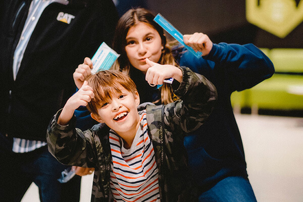 Two kids pose for a picture. They are giving the thumbs up and smiling.